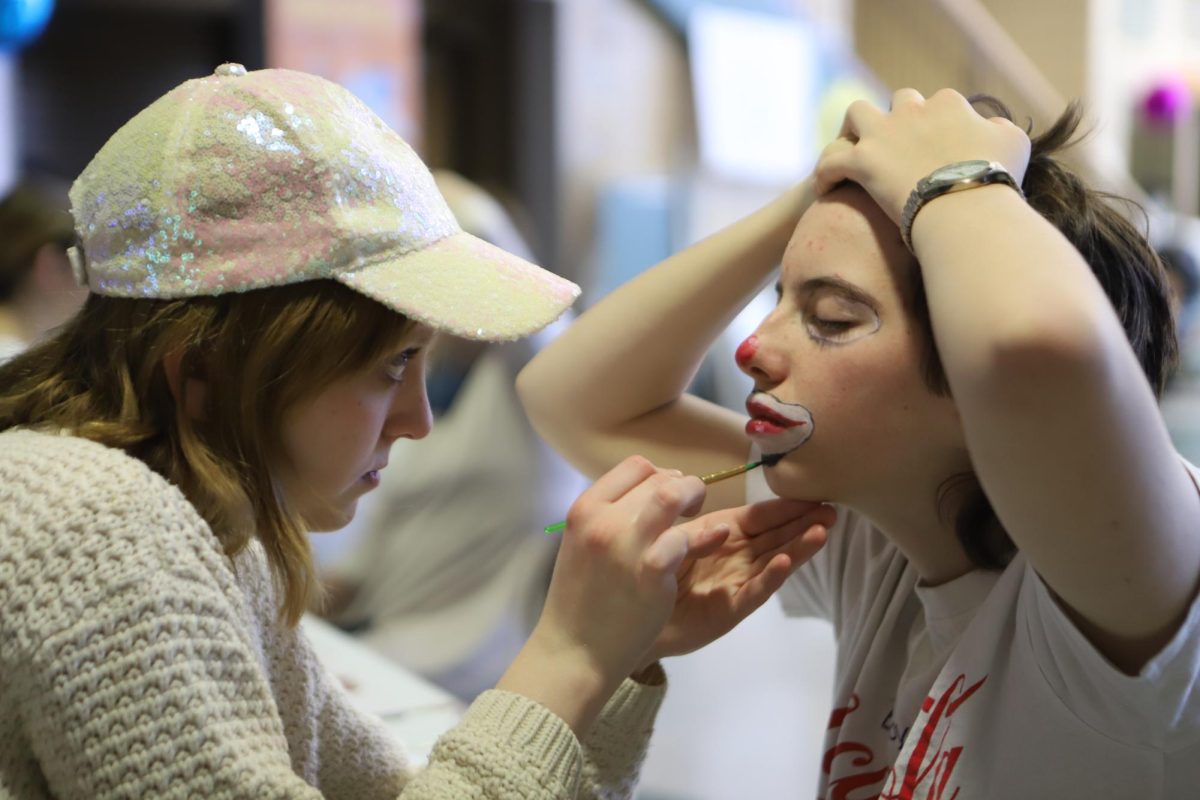 Junior Maggie Sullivan paints a clown design on junior Quincy Partington's face during lunch. For Peace Day, NAHS (National Honor Art Society) set up a face painting table for students to attend at lunch, which ended up garnering a large line of students. "I just really like that energy of a whole school just doing something fun, being at school without it being school," Sullivan said. 